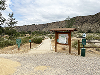 Kiosk near the trailhead near the parking area. View shows the trail leading acros the flower-covered floodpain with a cliff wall in the distance.